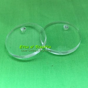 May include: Two clear, circular acrylic blanks with small holes for jewelry making or crafting. The blanks are on a green background. The text "Etch N' Scratch Laser Cutting & Engraving" is visible.