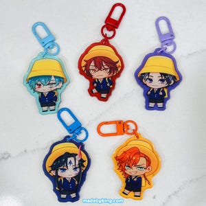 May include: Five anime-style character keychains. Each keychain features a different character wearing a yellow hat and a dark blue uniform. The keychains have colorful clasps in blue, red, purple, orange, and blue.