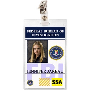 May include: A white plastic ID card with a blue border and the text "Federal Bureau of Investigation" in blue. The card has a photo of a woman with blonde hair, the text "FBI" in large blue letters, and the text "Jennifer Jareau SSA" in black letters.