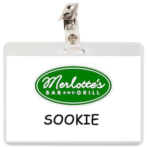 May include: A clear plastic name tag with a metal clip at the top. The tag displays the text "Merlotte's BAR AND GRILL" in green and white, with the name "SOOKIE" printed below in black.