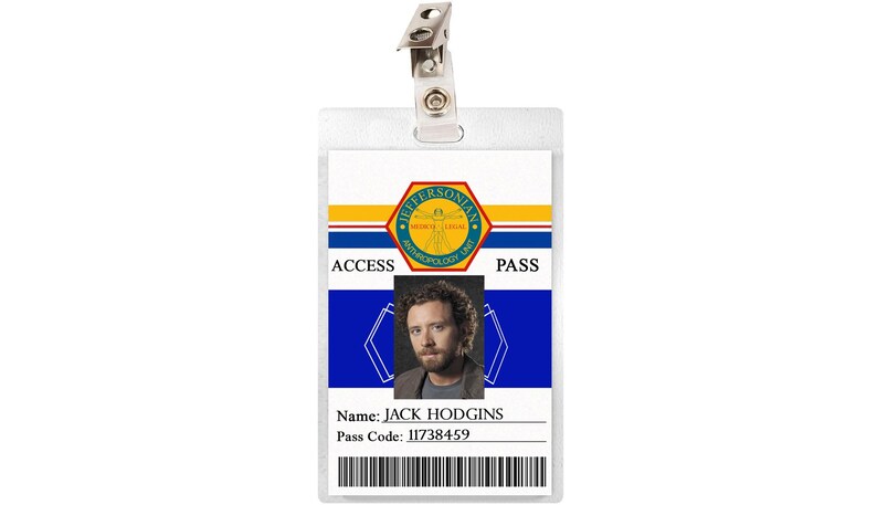 May include: A white plastic ID card with a blue and yellow design. The card has the text "ACCESS PASS" and a photo of a man with brown hair and a beard. The text "Name: JACK HODGINS" and "Pass Code: 11738459" is printed on the card.