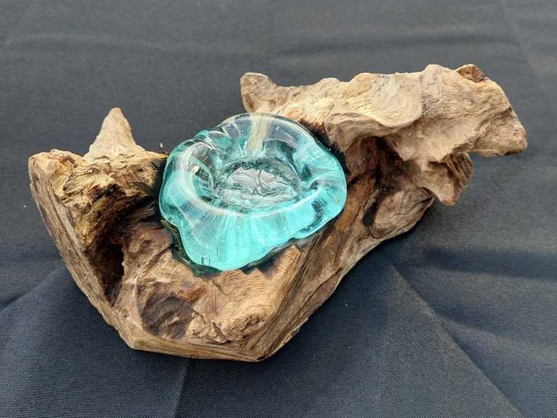 Pode incluir: Uma tigela de vidro azul-turquesa assenta em uma pe&ccedil;a natural e desgastada de madeira &agrave; deriva. A tigela tem uma forma &uacute;nica e org&acirc;nica e seria perfeita para uma vela ou uma planta pequena.