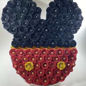 May include: A decorative Mickey Mouse head made of rolled paper roses. The ears are black, the face is red with yellow accents, and the center section is gold. Silver beads are interspersed throughout.