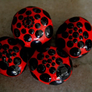 May include: Four smooth, round stones painted red with black polka dots. The dots are arranged in a circular pattern.