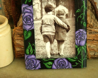 Pode incluir: Uma moldura de madeira preta com um design floral roxo e verde. A moldura contém uma foto de duas crianças de pé juntas.