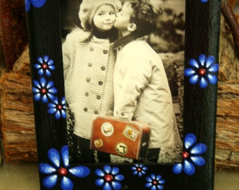 Pode incluir: Uma moldura de foto preta com um design floral azul e vermelho ao redor da borda. A moldura contém uma foto em preto e branco de duas crianças, uma menina e um menino, sorrindo um para o outro.