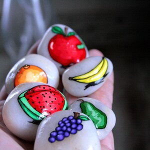 Puede incluir: Piedras pintadas a mano con dise&ntilde;os de frutas. Las piedras est&aacute;n pintadas con una sand&iacute;a, una naranja, un pl&aacute;tano, una pera, un racimo de uvas y una manzana.