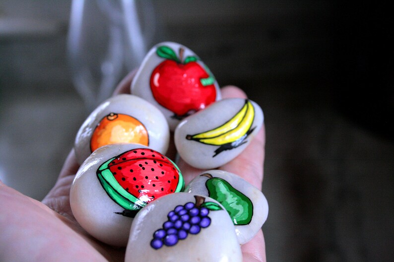 Puede incluir: Piedras pintadas a mano con dise&ntilde;os de frutas. Las piedras est&aacute;n pintadas con una sand&iacute;a, una naranja, un pl&aacute;tano, una pera, un racimo de uvas y una manzana.