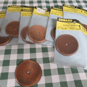 May include: A selection of antique copper finish backplates, each 5 cm in diameter, from the brand "ONWARD". The backplates are circular with a central hole and are packaged in clear plastic.