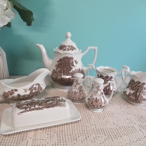May include: A set of brown and white porcelain teaware featuring a woodland scene design. The set includes a teapot, creamer, sugar bowl, gravy boat, butter dish, and two salt and pepper shakers.
