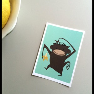 Carte de singe, carte postale aux couleurs vives avec le singe et la banane, dans les couleurs blanches, brunes, turquoise et jaune