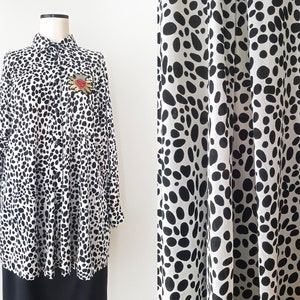 May include: A white and black dalmatian print long-sleeved button-up shirt with a black button closure and a small red and gold brooch.