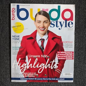 May include: A magazine cover featuring a woman wearing a red jacket and a white shirt with a tie. The magazine is titled "Burda Style" and has the words "Neue Töne", "Designerschnitt", "Unsere Näh", and "Highlights" on the cover.