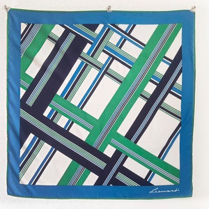 Può includere: Un foulard di seta bianco con un motivo geometrico di strisce verdi, blu e nere. Il foulard ha un bordo blu e la firma "Leonardi" nell'angolo in basso a destra.