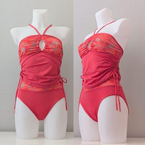 Può includere: Costume da bagno color corallo su manichino. Il top all'americana ha un dettaglio a forma di buco e una fascia fantasia. Gli slip a vita alta hanno lacci laterali regolabili. Il costume è progettato per l'abbigliamento da spiaggia.
