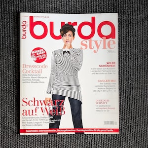 Könnte beinhalten: Ein Magazin-Cover mit einer Frau, die ein gestreiftes Hemd und Jeans trägt. Das Magazin heißt "Burda Style" und hat die Worte "Dresscode Cocktail", "Schwarz auf Weiß" und "Wilde Schönheit" auf dem Cover.
