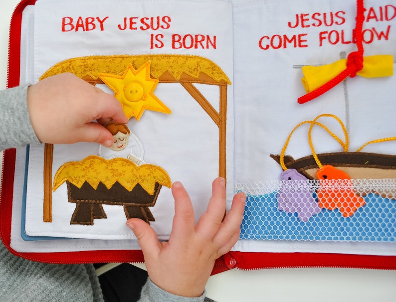 May include: A felt book for children with a yellow star, a manger scene with baby Jesus, and a blue net with two fish. The text on the book reads "Baby Jesus is born" and "Jesus said come follow".