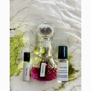May include: Three bottles of perfume oil labeled "Venus Nights". The bottles are clear glass with a pink liquid inside. The middle bottle is a larger, decorative bottle with a faceted stopper. The smaller bottles are roll-on bottles.