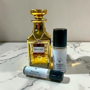May include: A gold-colored glass perfume bottle with a decorative chain and a square label reading Black Oud, accompanied by two small cylindrical fragrance oil vials with black caps and labels reading Black Oud Fragrance Oil.