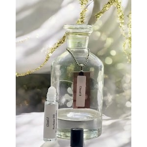 May include: A clear glass bottle with a silver chain and a tag that says "Cloud 9". Next to the bottle is a small roll-on bottle of perfume oil labeled "Cloud 9 Perfume Oil".