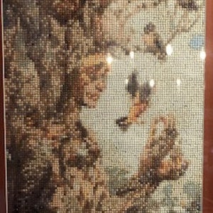 May include: A framed mosaic artwork depicting an underwater scene with coral and fish. The mosaic is composed of small, square tiles in shades of brown, beige, and orange, creating a textured and detailed image. The artwork is encased in a brown frame.