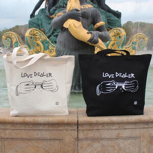 May include: Two tote bags, one white and one black, with the text "LOVE DEALER" and a graphic of hands rolling a joint.