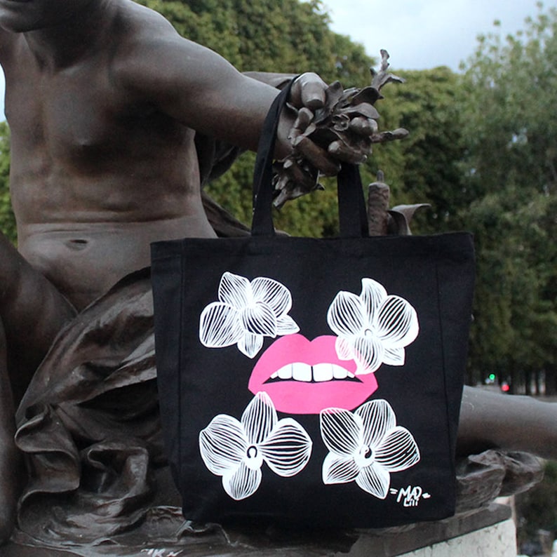 May include: Black tote bag with a pink lip print and white floral designs. The bag has the text "=MO= City" printed on the bottom.