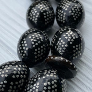 May include: A close-up of a black wooden prayer beads with silver dots. The beads are oval shaped and have a smooth, polished finish.