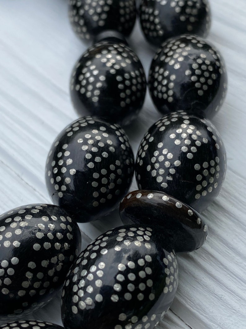 May include: A close-up of a black wooden prayer beads with silver dots. The beads are oval shaped and have a smooth, polished finish.