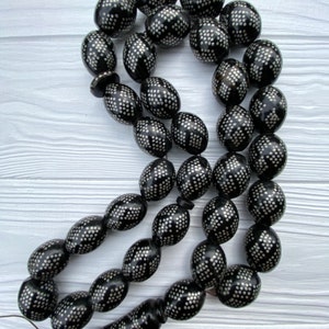 May include: A black prayer beads necklace with silver accents. The beads are oval shaped and have a geometric pattern.