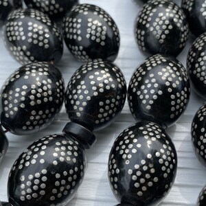 May include: A close-up of a black prayer beads necklace with silver dots. The beads are oval shaped and have a glossy finish.