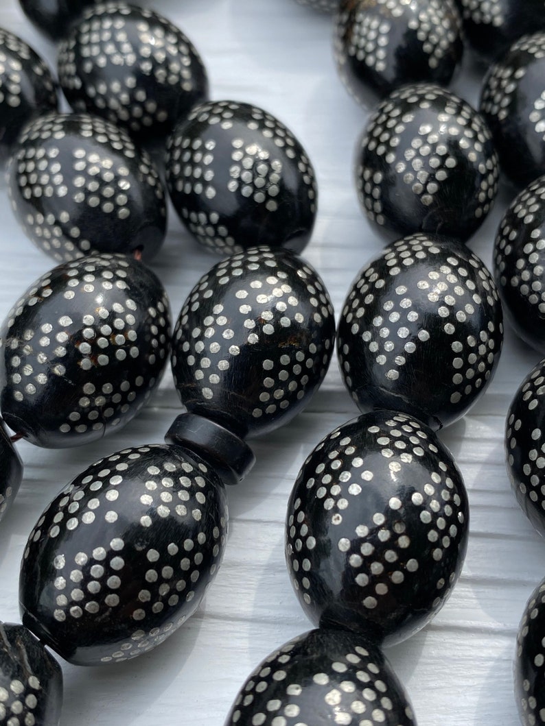May include: A close-up of a black prayer beads necklace with silver dots. The beads are oval shaped and have a glossy finish.