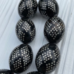 May include: A strand of black oval beads with a silver dot pattern. The beads are strung on a thin black cord.