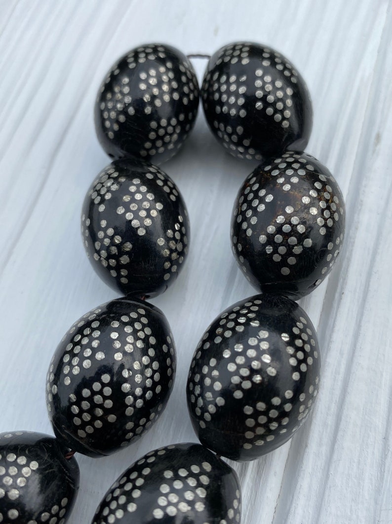 May include: A strand of black oval beads with a silver dot pattern. The beads are strung on a thin black cord.