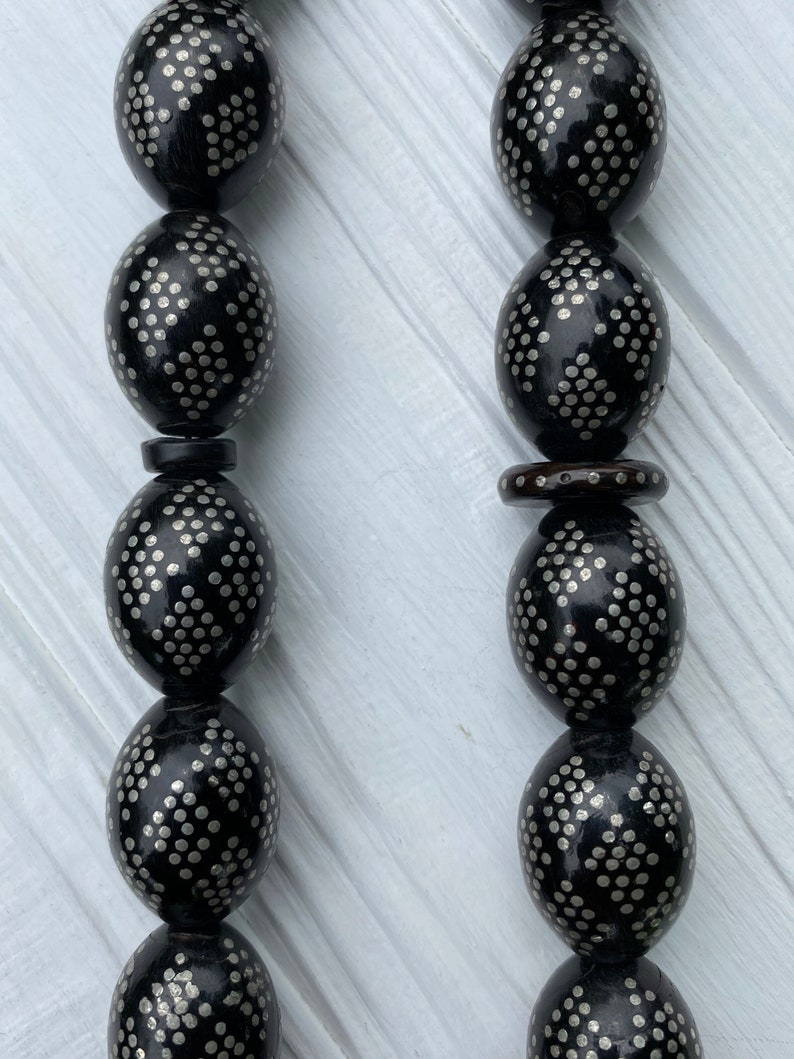 May include: A black prayer bead necklace with silver accents. The beads are oval shaped and have a repeating pattern of small silver dots.