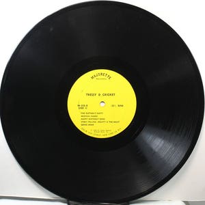 May include: A yellow vinyl record label with the text "Majorette Records" and "Tressy & Cricket" in black. The label also includes the text "M-108-8 Side II" and a list of songs: "The Birthday Party", "Musical Games", "Happy Birthday Song", "Story Telling: Beauty & The Beast", and "Going Home". The label also includes the text "33 1/3 RPM".