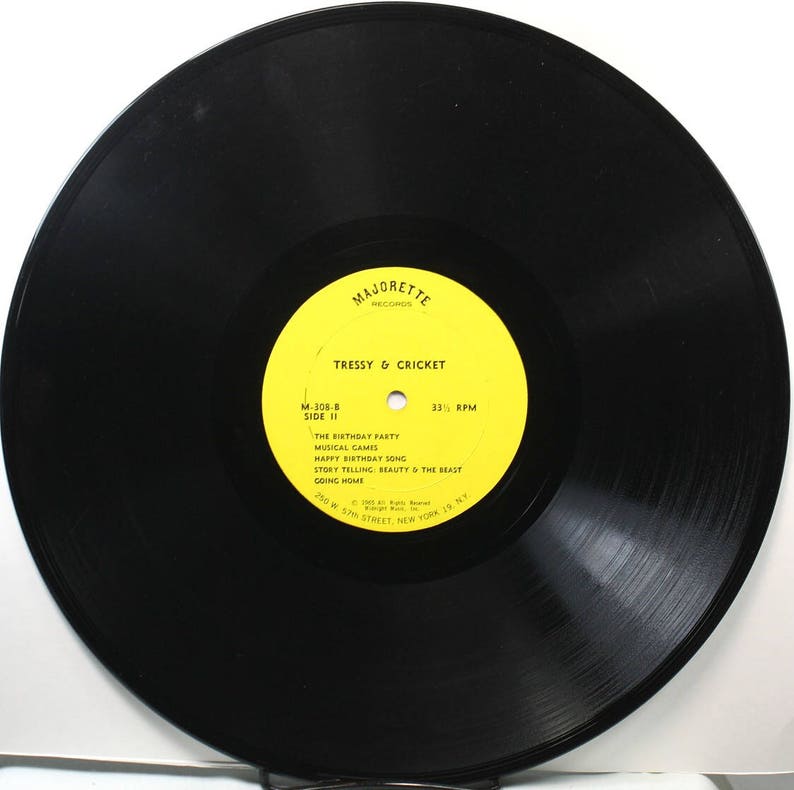 May include: A yellow vinyl record label with the text "Majorette Records" and "Tressy & Cricket" in black. The label also includes the text "M-108-8 Side II" and a list of songs: "The Birthday Party", "Musical Games", "Happy Birthday Song", "Story Telling: Beauty & The Beast", and "Going Home". The label also includes the text "33 1/3 RPM".