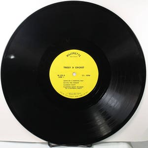May include: A black vinyl record with a yellow label. The label has the text "Majorette Records" and "Tressy & Cricket" in black text. The record is 33 1/3 RPM and has the following song titles: "Going on a Shopping Trip", "Buying the Present", "Glamour Party", "Planning What to Wear to a Birthday Party".