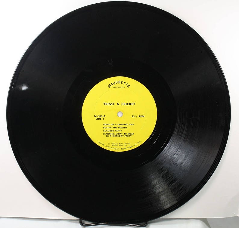 May include: A black vinyl record with a yellow label. The label has the text "Majorette Records" and "Tressy & Cricket" in black text. The record is 33 1/3 RPM and has the following song titles: "Going on a Shopping Trip", "Buying the Present", "Glamour Party", "Planning What to Wear to a Birthday Party".