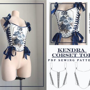 May include: A white corset top with a blue floral design, detailed with dark blue ribbon ties and straps. The corset is shown on a mannequin. The text "KENDRA CORSET TOP PDF SEWING PATTERN" is displayed.