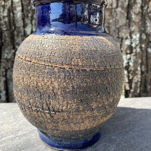 May include: A dark blue ceramic vase with a textured, cracked surface. The vase has a round body and a slightly flared rim.