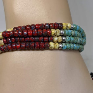May include: Multi-colored beaded bracelet with red, yellow, and blue beads. The bracelet is made of small, round beads and is layered to create a unique and colorful design.