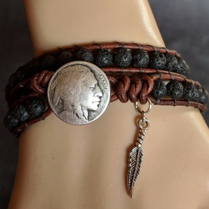 Pu&ograve; includere: Un braccialetto in pelle marrone con perline di lava nera e un ciondolo a forma di moneta da nickel con la testa di un indiano in argento. Un ciondolo a forma di piuma d'argento &egrave; appeso al braccialetto.