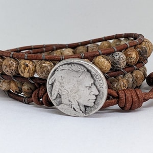 May include: A brown leather wrap bracelet with brown and white stone beads and a silver buffalo nickel charm.