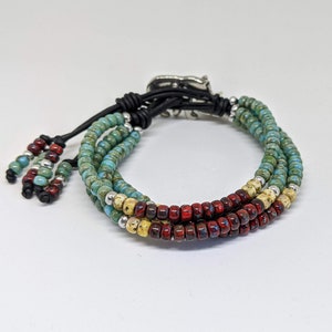 May include: A multi-strand bracelet with turquoise, red, and cream colored beads. The bracelet has a silver clasp and black leather ties.