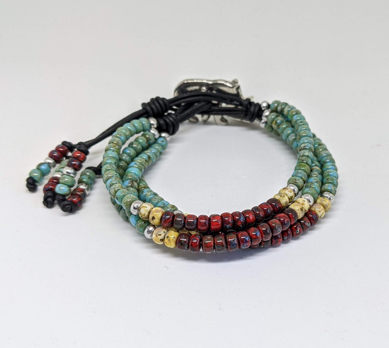 May include: A multi-strand bracelet with turquoise, red, and cream colored beads. The bracelet has a silver clasp and black leather ties.