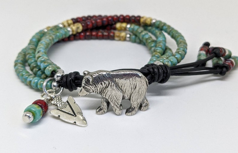 May include: A multi-strand bracelet with turquoise, red, and beige beads. The bracelet has a silver bear charm and a silver arrowhead charm.