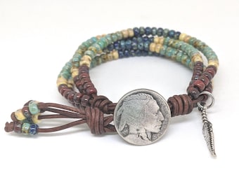 Può includere: Un braccialetto avvolgente a tema nativo americano. Il braccialetto presenta una moneta d'argento con il profilo di un nativo americano, un piccolo ciondolo a forma di piuma d'argento e perline multicolori nelle tonalità del blu, marrone e giallo. Il braccialetto è in pelle.