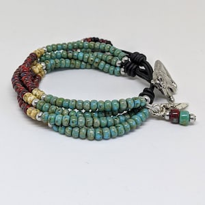 May include: Multi-strand bracelet with turquoise, cream, and red beads. The bracelet has a leather closure with a silver charm and a feather dangle.