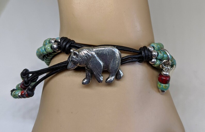 May include: A leather bracelet with a silver bear charm and turquoise and red beads.